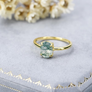 May include: A gold ring with a green moss agate gemstone. The ring is on a blue velvet background.