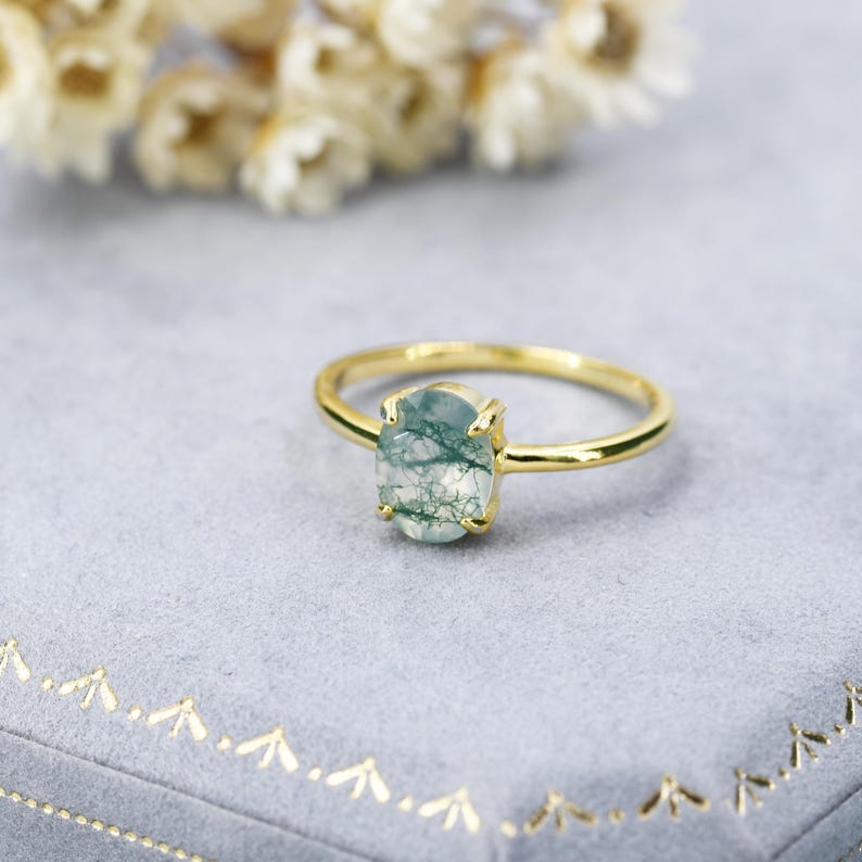 May include: A gold ring with a green moss agate gemstone. The ring is on a blue velvet background.