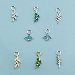 Pode incluir: Uma coleção de pingentes de folhas em tons de prata e dourado. Alguns apresentam cristais transparentes, esmalte verde ou um design de folha de hera azul-esverdeada. Cada pingente tem um pequeno laço para fixação.
