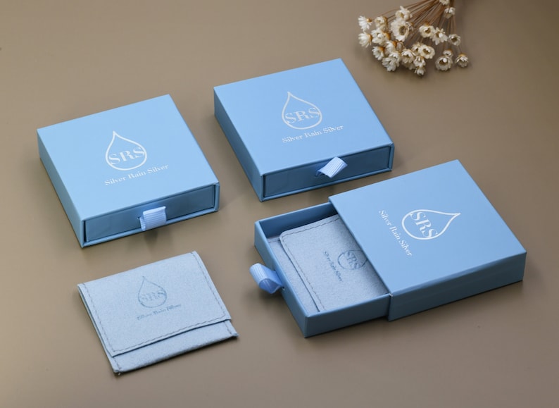 May include: Four light blue boxes with a white raindrop logo and the text "Silver Rain Silver". The boxes have a drawer that slides out to reveal a small, light blue pouch with the same logo.