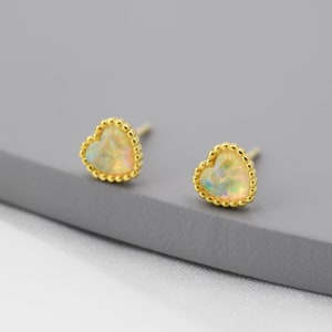 May include: A pair of gold heart-shaped earrings with opal stones. The earrings have a beaded border.