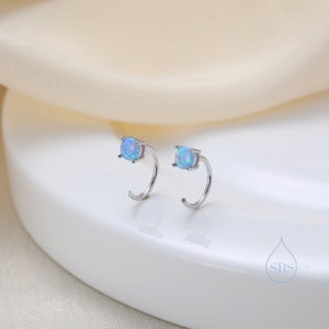 Puede incluir: Un par de pendientes de aro de plata con una piedra de ópalo azul claro en cada aro.