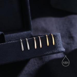 May include: A set of six small, thin, curved earrings in different metal finishes: silver, rose gold, and gold. The earrings are displayed in a velvet-lined box.