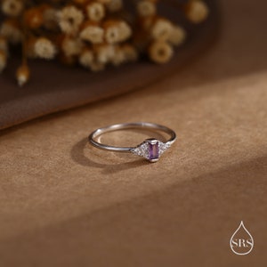 Puede incluir: Un anillo de plata con una piedra preciosa p&uacute;rpura y peque&ntilde;as piedras preciosas transparentes engastadas en forma de tri&aacute;ngulo.