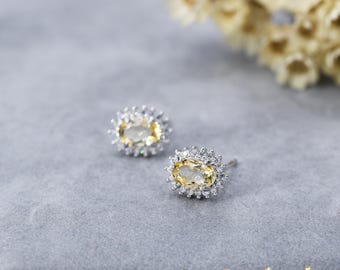 May include: A pair of silver earrings with a yellow oval gemstone surrounded by smaller clear gemstones.