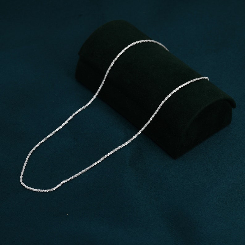 Puede incluir: Un collar de cadena de plata sobre una superficie de terciopelo verde oscuro.