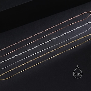 May include: A collection of five delicate necklaces arranged diagonally. The set includes three metal chains with small evenly spaced beads in rose gold, silver, and gold tones, alongside two smooth, thin, solid metal chains in silver and gold.