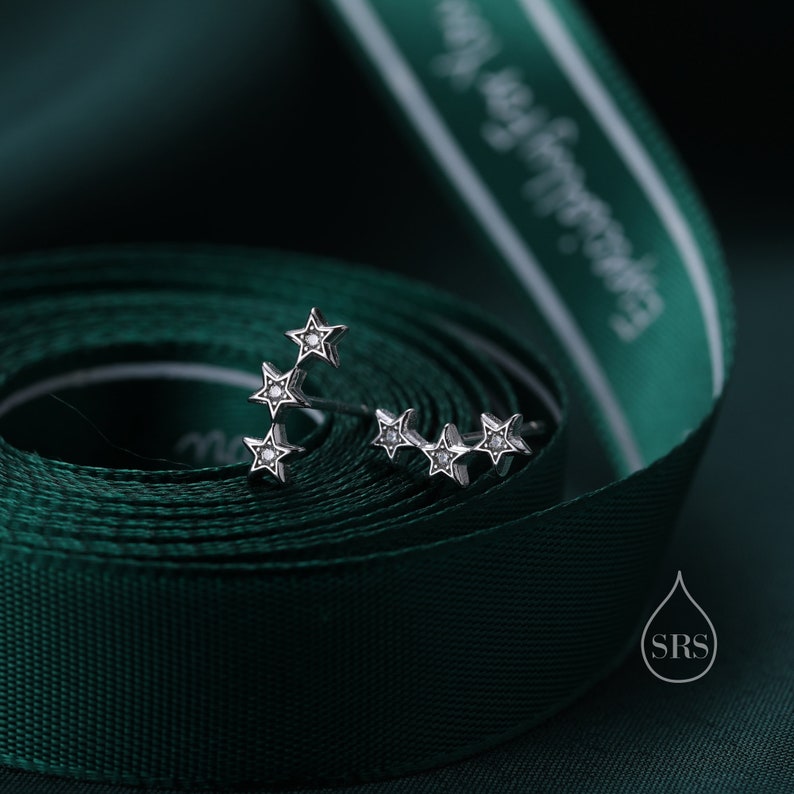 May include: A pair of silver star earrings with small clear stones set in each star. The earrings are on a green ribbon.