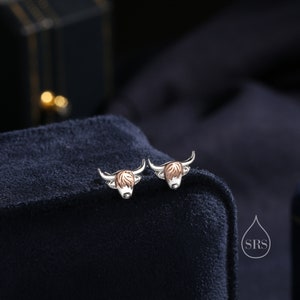 May include: A pair of silver earrings with a Highland Cow design. The cow's head is made of rose gold and the rest of the earring is silver.
