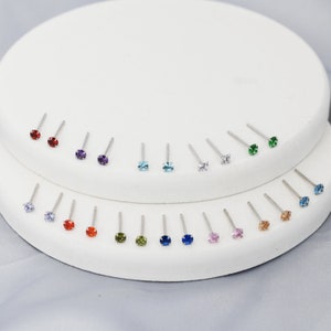 Puede incluir: Una muestra de 18 pares de pendientes de plata con piedras preciosas de varios colores. Las piedras preciosas incluyen rojo, morado, azul, verde y rosa.