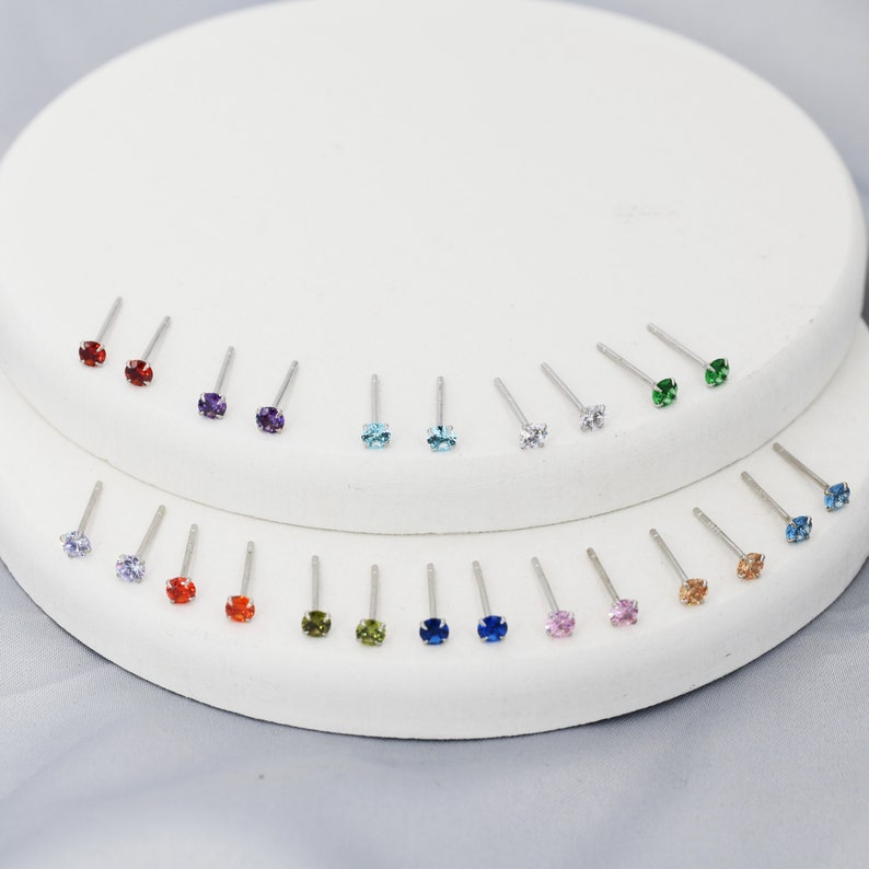 Puede incluir: Una muestra de 18 pares de pendientes de plata con piedras preciosas de varios colores. Las piedras preciosas incluyen rojo, morado, azul, verde y rosa.