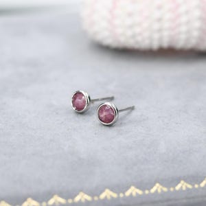 Puede incluir: Un par de pendientes de botón de plata con detalles de piedras preciosas rosas.