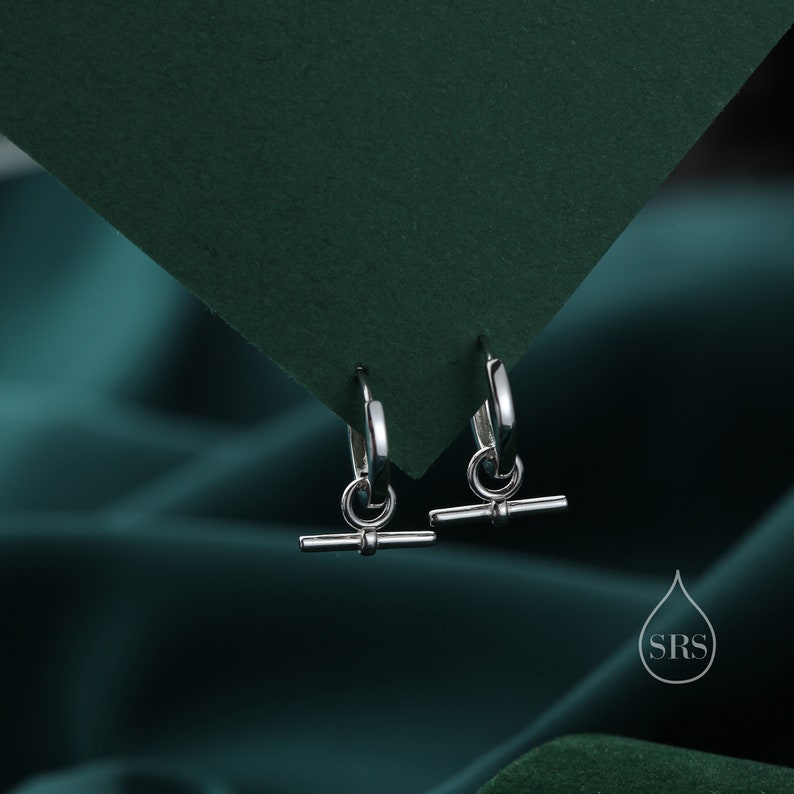 May include: A pair of silver hoop earrings with a small, horizontal bar hanging from each hoop.