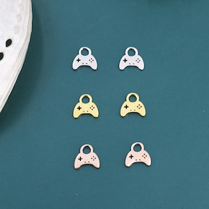 May include: Six small charms in the shape of video game controllers. Two are silver, two are gold, and two are rose gold. Each charm has a loop at the top and a cross and four dots on the controller.