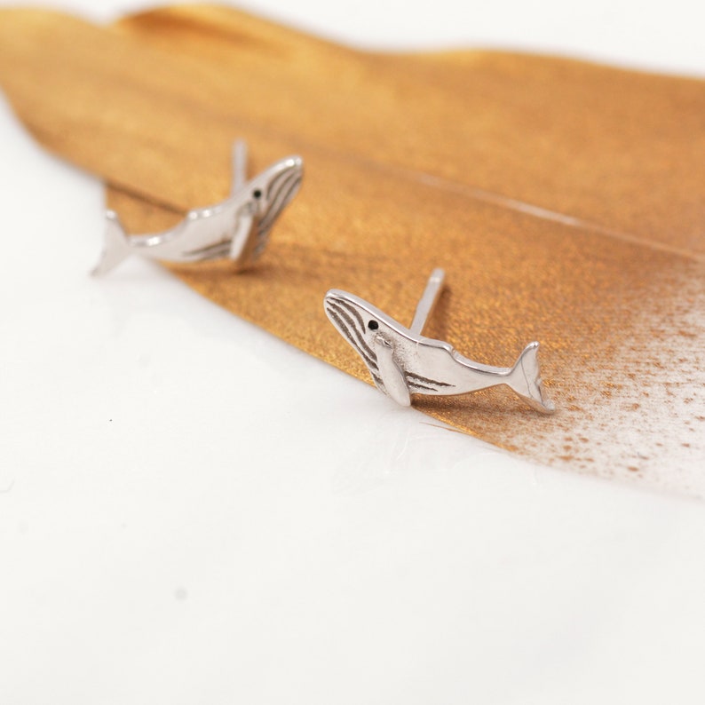 May include: A pair of silver whale stud earrings. The whales are facing to the right and have a detailed design.