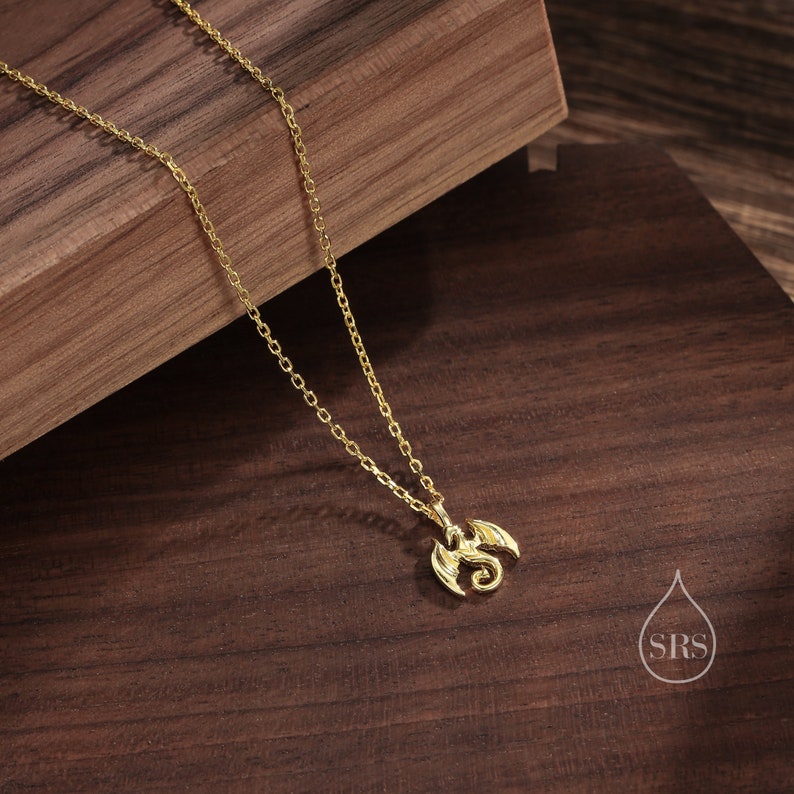 May include: A gold chain necklace with a small, detailed dragon pendant. The necklace is on a wooden surface.