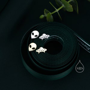 Könnte beinhalten: Drei Paar silberne und goldene Ohrringe mit Alien- und UFO-Motiven auf einem grünen Band. Die Ohrringe sind klein und filigran.