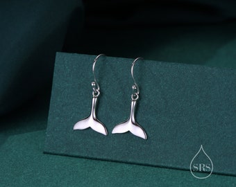 May include: A pair of silver dangle earrings with a whale tail design. The earrings are on a green background.