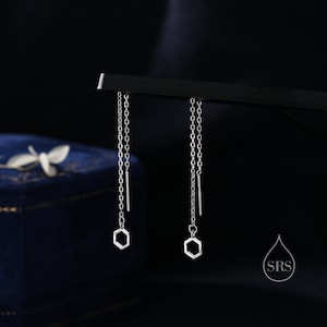May include: A pair of silver chain earrings with hexagon-shaped charms hanging from the ends. The earrings are displayed on a black surface.