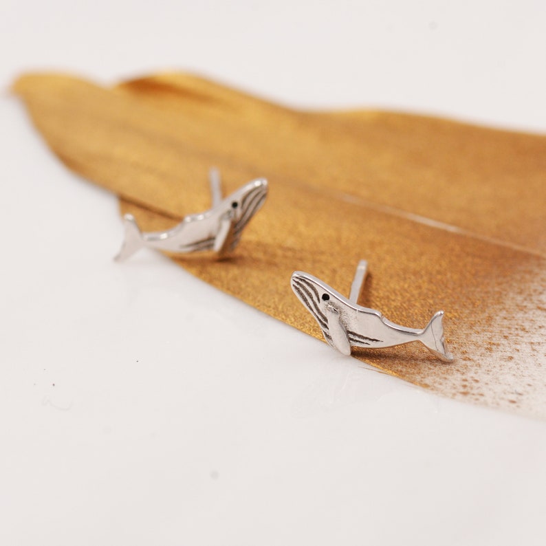 May include: A pair of silver whale stud earrings. The whales are facing to the right and have a detailed design.