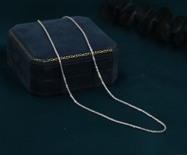 Puede incluir: Un collar de cadena de plata con un dise&ntilde;o delicado y brillante. La cadena est&aacute; colocada sobre una caja de terciopelo azul.