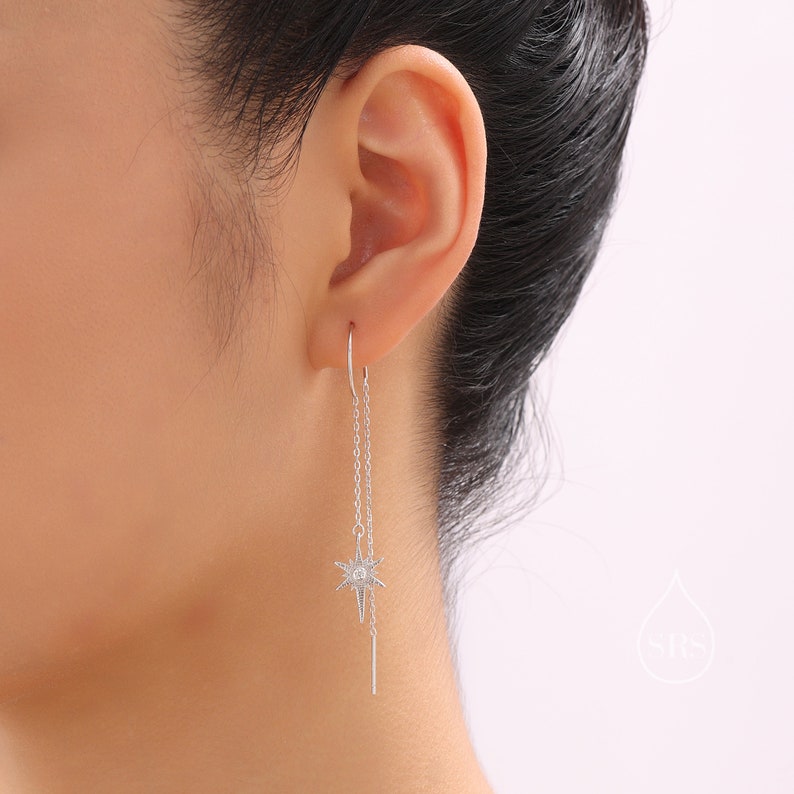 May include: Silver dangle earrings with a star charm and a chain. The star charm has a small clear stone in the center.