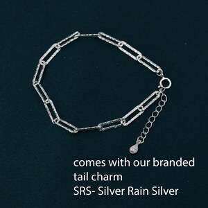 May include: A silver chain bracelet with a textured finish. The bracelet has a lobster clasp and a small silver charm with the text "SRS - Silver Rain Silver" on it.