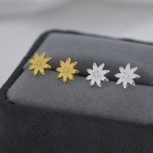 May include: A set of four earrings featuring a flower design. Two earrings are gold and two are silver.