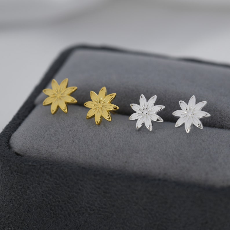 May include: A set of four earrings featuring a flower design. Two earrings are gold and two are silver.