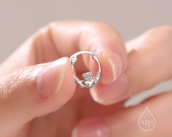 Może przedstawiać: Srebrne kolczyki koła z wzorem Claddagh. Claddagh przedstawia dwie dłonie trzymające serce z koroną na górze.