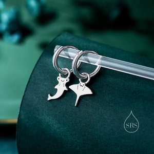 May include: A pair of silver hoop earrings with a small silver hammerhead shark charm on one earring and a silver manta ray charm on the other earring.