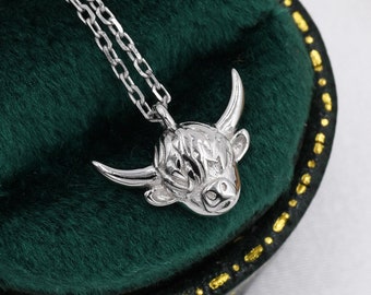 May include: A silver necklace featuring a Highland cow head pendant. The pendant is detailed with a textured fur design. The necklace is displayed on a green velvet background.