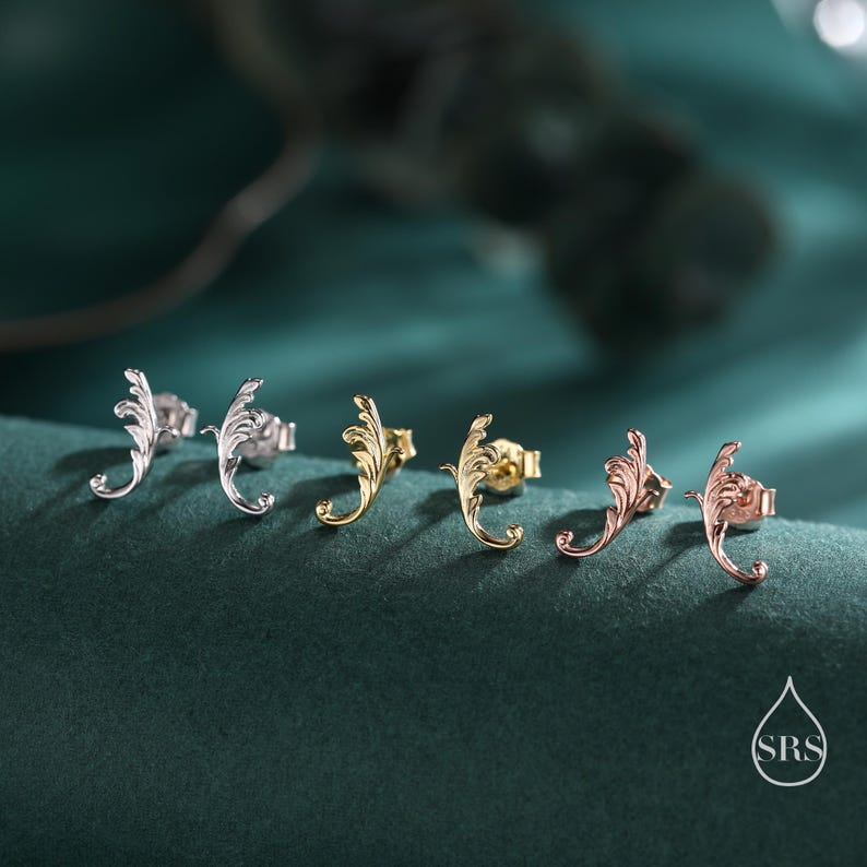 May include: Five pairs of silver, gold, and rose gold earrings with a delicate, ornate leaf design. The earrings are displayed on a green surface.