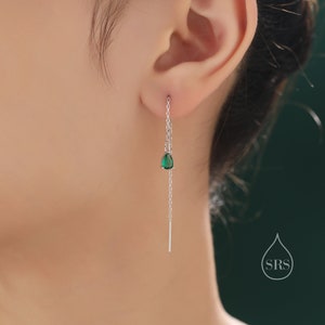 May include: A silver threader earring with a dangling emerald green teardrop-shaped gemstone. The earring is shown worn on an ear, with the chain extending downward. The earring has a simple, elegant design.