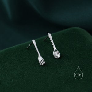 May include: A pair of silver earrings, one shaped like a fork and the other shaped like a spoon.
