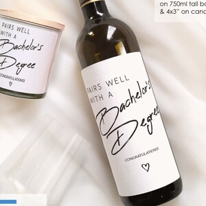 K&ouml;nnte beinhalten: Eine wei&szlig;e Weinflasche mit einem schwarz-wei&szlig;en Etikett, auf dem "Pairs well with a Bachelor's Degree. Congratulations!" steht. Eine wei&szlig;e Kerze mit einem schwarz-wei&szlig;en Etikett, auf dem "Pairs well with a Bachelor's Degree. Congratulations!" steht. Ein klares Weinglas.