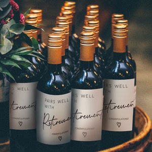 Peut inclure: Un groupe de bouteilles de vin avec des &eacute;tiquettes personnalis&eacute;es qui disent "Pairs Well With Retirement" et "Congratulations!" dans une police d'&eacute;criture manuscrite. Les &eacute;tiquettes sont beiges avec du texte brun et un petit symbole de c&oelig;ur.