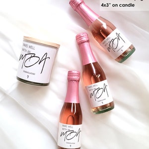 May include: Three mini bottles of pink champagne with white labels that say "Pairs well with an MBA" and "Congratulations!"  A white candle with a wooden lid and a label that says "Pairs well with an MBA" and "Congratulations!"