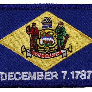 May include: A blue and yellow embroidered patch featuring the state seal of Delaware. The seal depicts a farmer holding a plow and a soldier holding a musket, with a ship in the background. The text "DECEMBER 7, 1787" is embroidered below the seal.