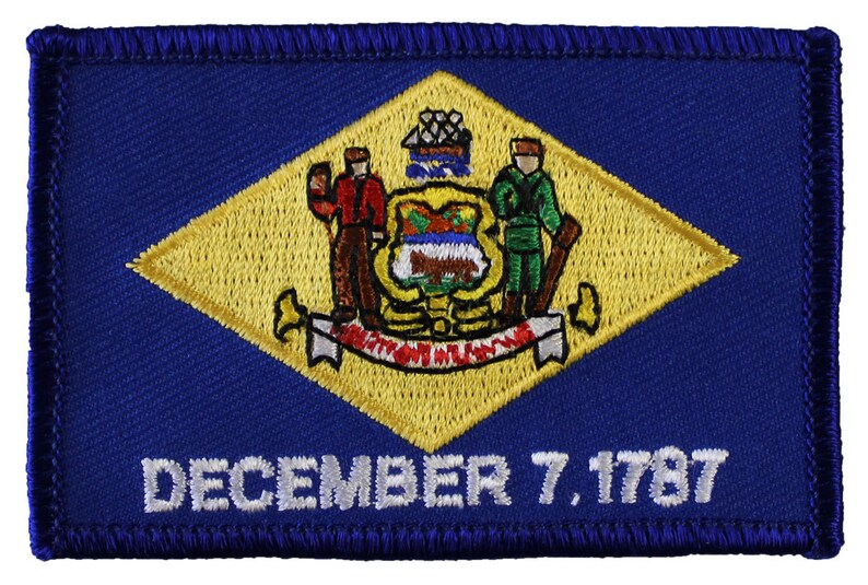 May include: An embroidered patch in blue and yellow featuring the state seal of Delaware. The seal depicts a farmer holding a plough and a soldier holding a musket, with a ship in the background. The text "DECEMBER 7, 1787" is embroidered below the seal.