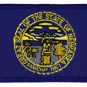 May include: A blue fabric patch with the state seal of Nebraska. The seal is a circle with the words "Great Seal of the State of Nebraska" around the edge. Inside the circle is a depiction of a tree, a river, and a sun.
