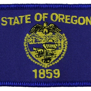 May include: A blue embroidered patch with the words "STATE OF OREGON" and the state seal in yellow. The seal features a beaver, a wagon wheel, and a mountain range. The year "1859" is also embroidered in yellow.