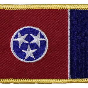 May include: A red and blue embroidered patch with a white circle containing three white stars and a blue circle in the center. The patch has a gold border.