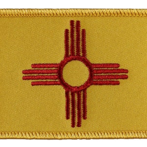 May include: A yellow embroidered patch with the state flag of New Mexico. The flag features a red Zia symbol, a traditional symbol of the Zia Pueblo people.