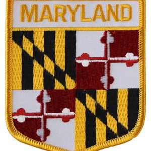 May include: A yellow, black, and red embroidered patch with the word "MARYLAND" in yellow lettering on a white background. The patch is shaped like a shield and has a gold border.