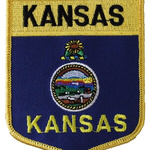 May include: A blue and yellow embroidered patch with the state seal of Kansas and the word "KANSAS" written twice.