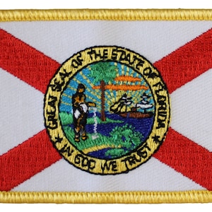 May include: Embroidered patch featuring the state flag of Florida. The flag is white with a red diagonal cross and the state seal in the center. The seal depicts a sun, a tree, a man pouring water from a pitcher, a steamboat, and the words "Great Seal of the State of Florida" and "In God We Trust".