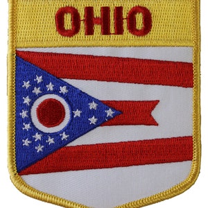 May include: An embroidered patch featuring the Ohio state flag. The flag is a white field with a blue triangle in the upper left corner. The triangle contains a circle with a red center and 17 white stars. The flag also has three red stripes across the bottom. The patch is bordered in gold and has the word "OHIO" in red letters at the top.