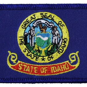 May include: Embroidered patch featuring the state seal of Idaho. The seal depicts a blue background with a mountain range, a sun, and a bald eagle. The text "Great Seal of the State of Idaho" is written around the seal. The patch is blue with yellow and red accents.