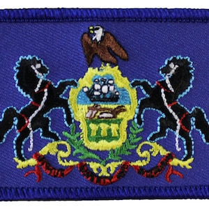 May include: A blue embroidered patch featuring the state seal of Pennsylvania. The seal depicts a ship, an eagle, and two horses supporting a shield with the letters "Virtue, Liberty, and Independence" on a scroll.